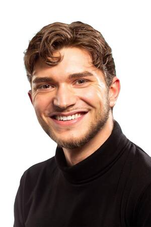 Ein lächelnder Mann mit lockigem Haar trägt einen schwarzen Rollkragenpullover vor einem weißen Hintergrund.
