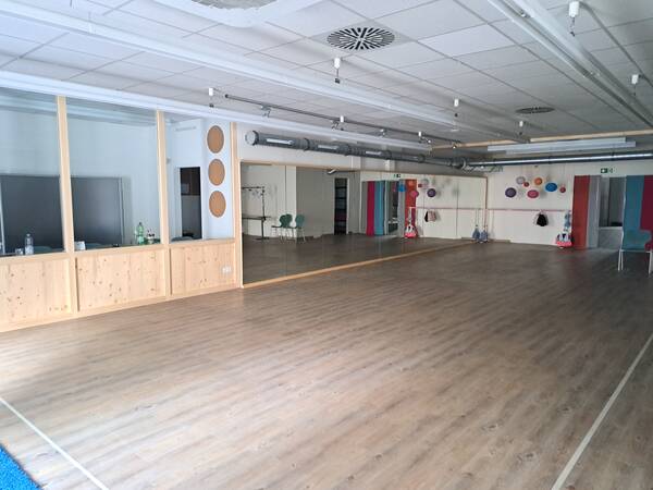 Ein großer, leerer Raum mit Holzboden, Spiegelwand und farbigen Dekorationen an der Wand.
